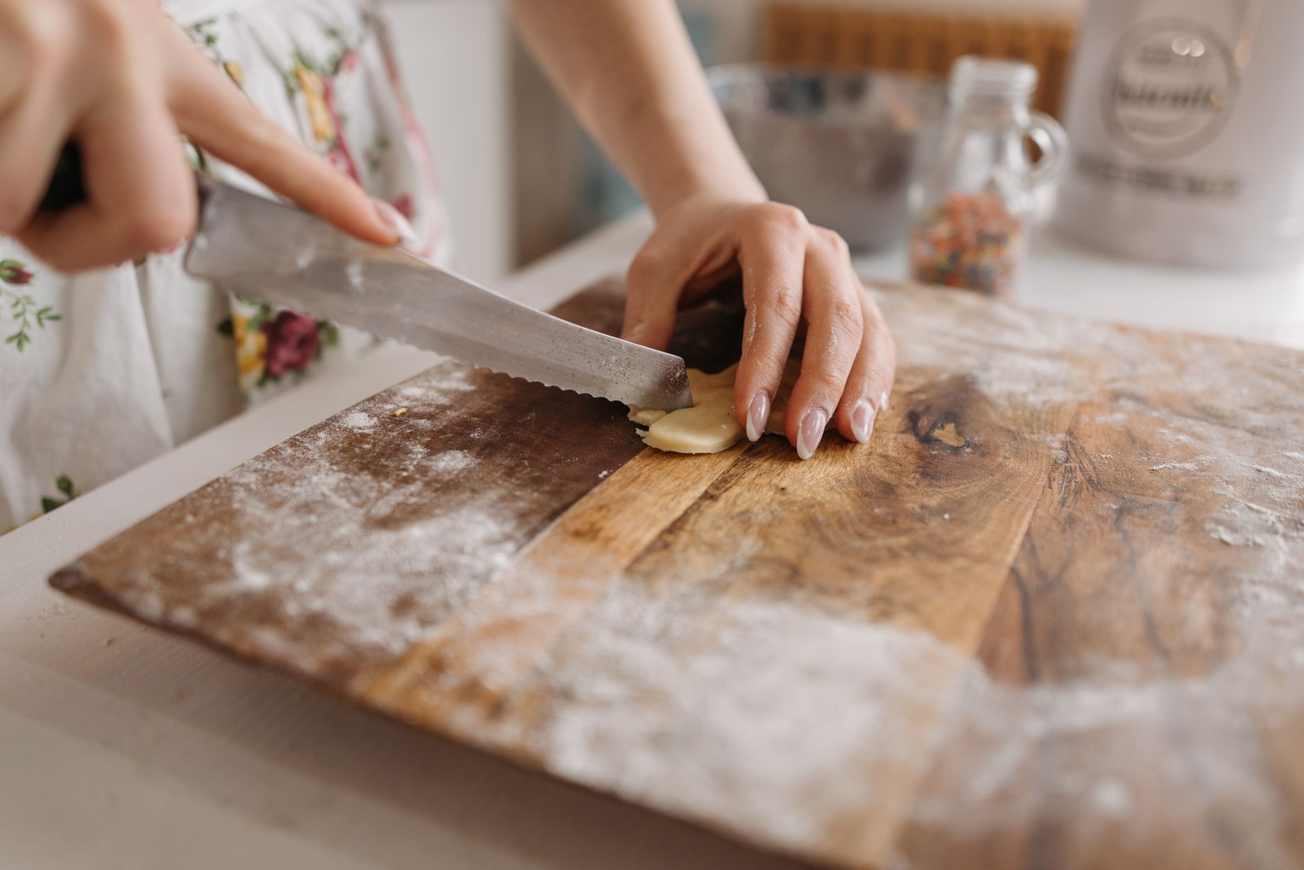 Hands slice a roll of dough on a flour-dusted wooden board.